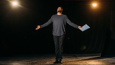 Ein junger Schauspieler steht mit einem Skript auf einer Bühne. | Bild: colourbox.com