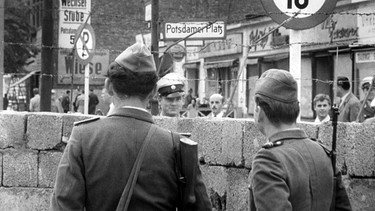 Volkspolizisten aus der DDR wechseln am 23.08.1961 über die Berliner Mauer am Potsdamer Platz ein Lächeln mit einem Polizeibeamten aus Westberlin. | Bild: picture-alliance/ dpa | UPI