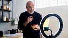 Senior man with fruit bowl vlogging through smart home in kitchen | Bild: picture alliance / Westend61 | Giorgio Fochesato