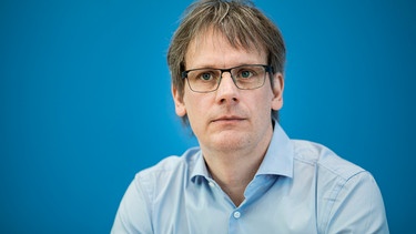 Felix Kolb hat graue Haare und eine graue Brille. Er sitzt vor einem blauen Hintergrund, eine Wand der Bundespressekonferenz.  | Bild: picture alliance / photothek | Florian Gaertner