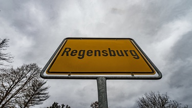 ARCHIV - 22.02.2017, Bayern, Regensburg: Dunkle Wolken ziehen über dem Ortsschild von Regensburg (Bayern).  Nirgendwo lebten 2022 so viele Menschen allein wie in der Großstadt in der Oberpfalz, teilte das Unternehmen GfK in Nürnberg am Dienstag mit. Der Anteil der Einpersonenhaushalte lag demnach in der Stadt bei 52,7 Prozent. . (zu dpa: «Regensburg stimmt gegen eine Stadtbahn») Foto: Armin Weigel/dpa +++ dpa-Bildfunk +++ | Bild: dpa-Bildfunk/Armin Weigel