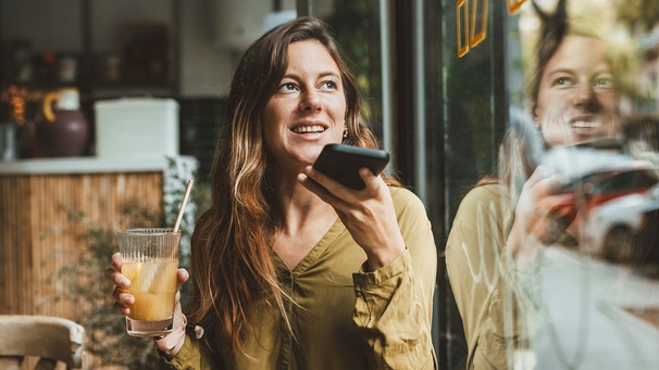 Eine Frau sitzt in einem Café und spricht eine Sprachnachricht in ihr Smartphone | Bild: picture alliance / Westend61 | Joseffson