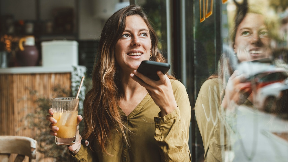 Eine Frau sitzt in einem Café und spricht eine Sprachnachricht in ihr Smartphone | Bild: picture alliance / Westend61 | Joseffson