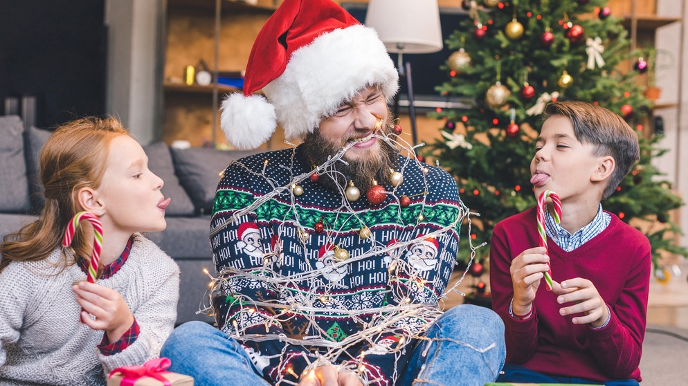 Bescherung unter dem Weihnachtsbaum: ein Mädchen, ein Junge und ein junger Mann mit Bart, der mit einer Lichterkette gefesselt wurde ... | Bild: colourbox.com