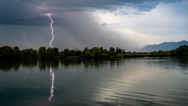 Eine Gewitterfrontzieht mit einem einschlagendem Blitz über einem Alpensee in Bayern  auf. | Bild: stock.adobe.com/Vincent