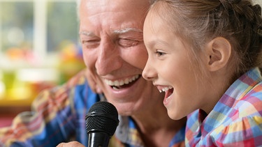 Ein Großvater singt mit seiner Enkelin Karaoke, beide lachen. | Bild: stock.adobe.com/aletia2011