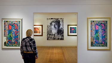 Friedensreich Hundertwasser: Ausstellungsbesucherin betrachtet Portrait des Künstlers und Bilder - Symbolbild  | Bild: picture alliance_dpa_Axel Heimken