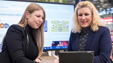 Rebekka Seelmann (links) und Anja Myriam Anton (rechts) in einer Besprechung zum didacta-Auftritt an einem iPad. | Bild: WDR/Taimas Ahangari