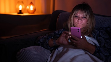 Eine Frau sitzt im Bett und blickt auf ihr Smartphone.  | Bild: streetsfilm 