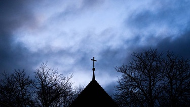 Dunkle Wolken ziehen über das Kreuz einer evangelischen Kirche auf.  | Bild: picture-alliance/dpa