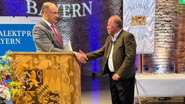 Bayerischer Dialektpreis 2024 für Stefan Frühbeis: Finanzminister Albert Füracker (CSU) überreicht die Auszeichnung an Frübeis (rechts). | Bild: Gabriel Wirth
