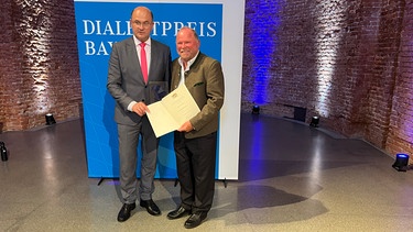 Bayerischer Dialektpreis 2024 für Stefan Frühbeis: Finanzminister Albert Füracker (CSU) überreicht die Auszeichnung an Frübeis (rechts). | Bild: Gabriel Wirth