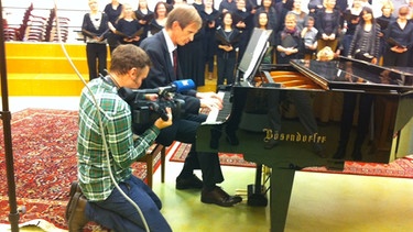 Weihnachtssingen 2012: Albrecht Hesse spielt Klavier und wird dabei gefilmt, im Hintergrund ist der BR-Chor | Bild: privat