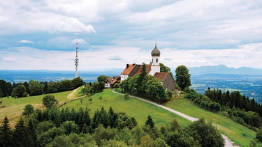 Hohenpeißenberg im Pfaffenwinkel: im Hintergrund zu sehen ist der Sender Hohenpeißenberg, der für die Fernseh- und Radioübertragung eine wichtige Funktion hat. Im Vordergrund befindet sich die Wallfahrtskapelle Maria Himmelfahrt mit Wirtschaftsgebäuden. | Bild: Adobe Stock /  ©aBSicht