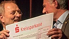 Martin Fogt und Andreas Heringer von der Kolpingsfamilie Ebersberg halten großen Spendenscheck hoch | Bild: BR/Andreas Dirscherl